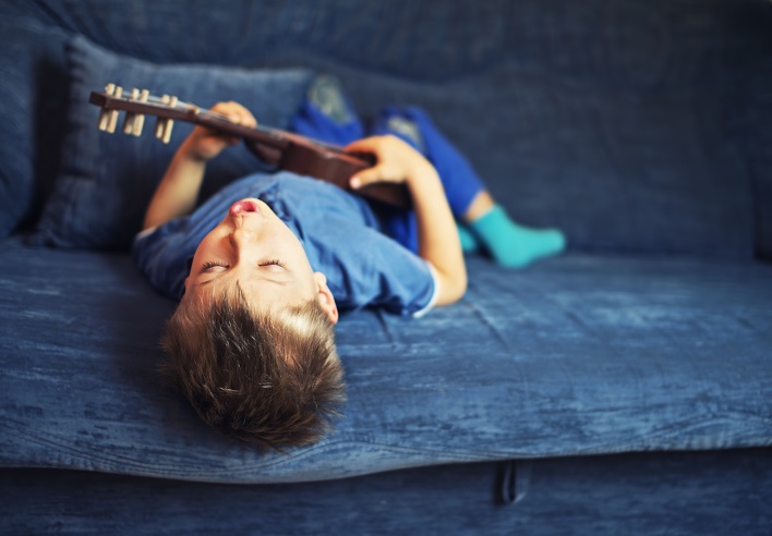 Little boy playing the guitar and singing on the couch.